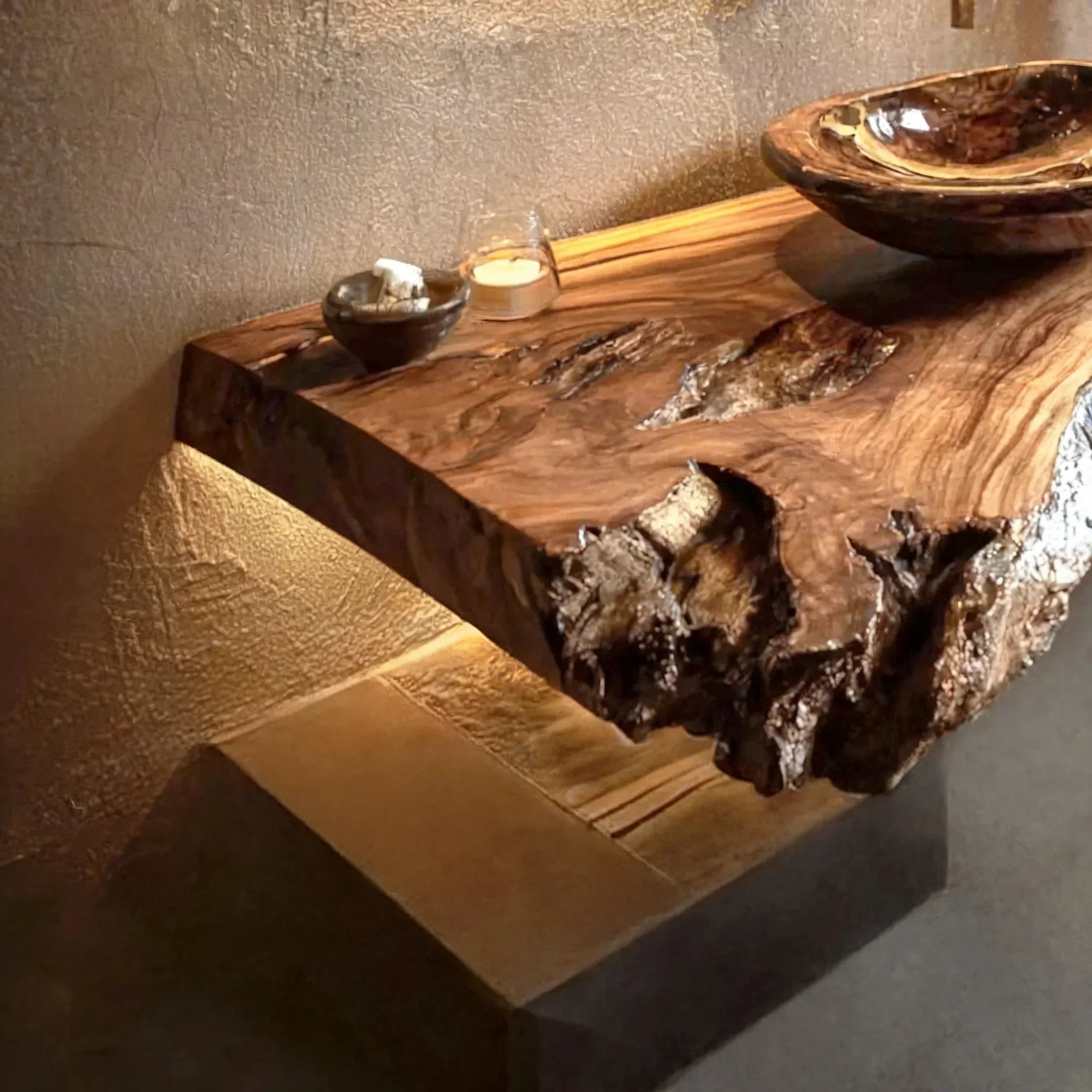 Floating live edge wooden desk with natural finish, decorative bowl, and warm lighting.