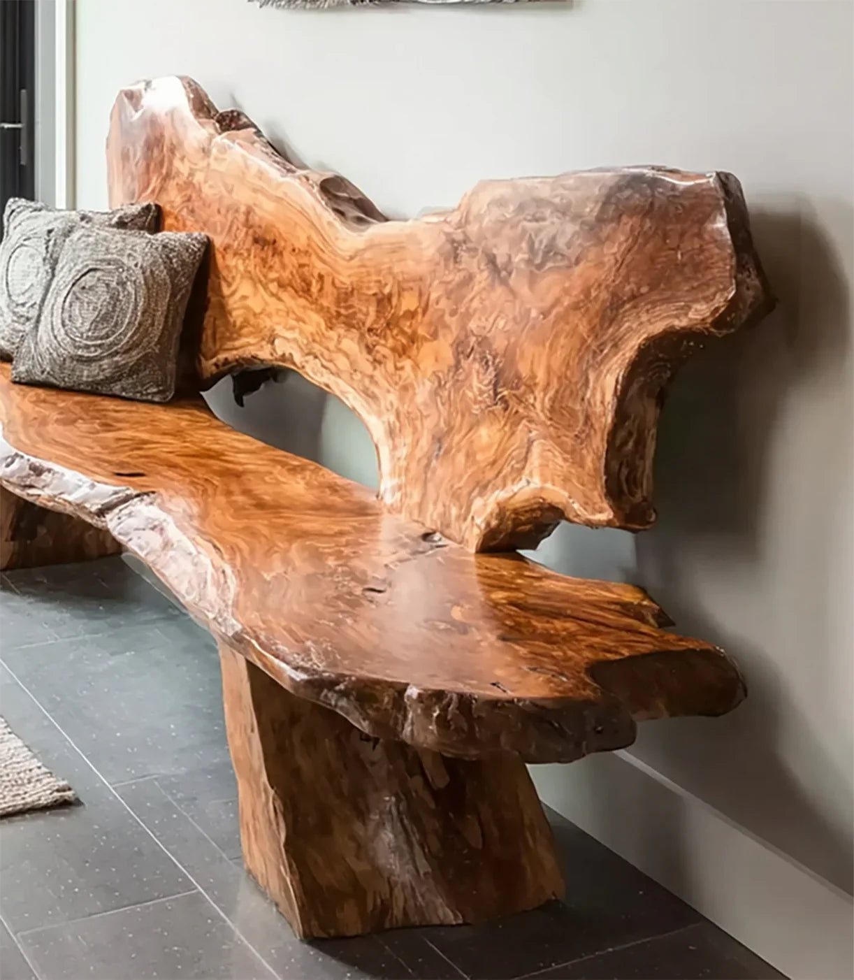 Natural wood slab bench with organic shapes and two textured gray pillows against a light wall