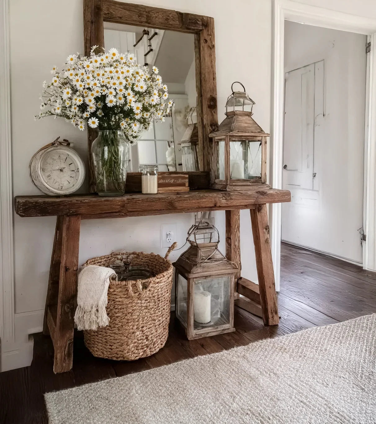 Rustic wooden console table with daisy bouquet, vintage clock, lanterns, woven basket, and mirror in cozy hallway