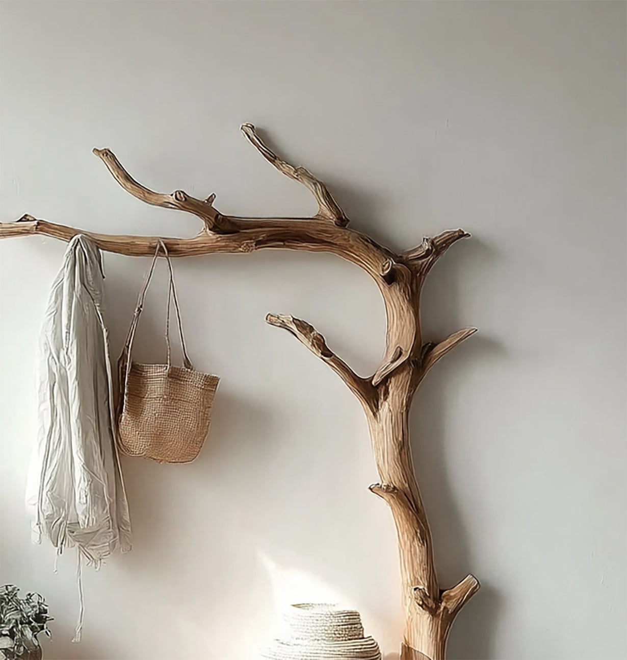 Rustic branch coat rack mounted on wall with hanging white jacket and woven bag in minimalist interior