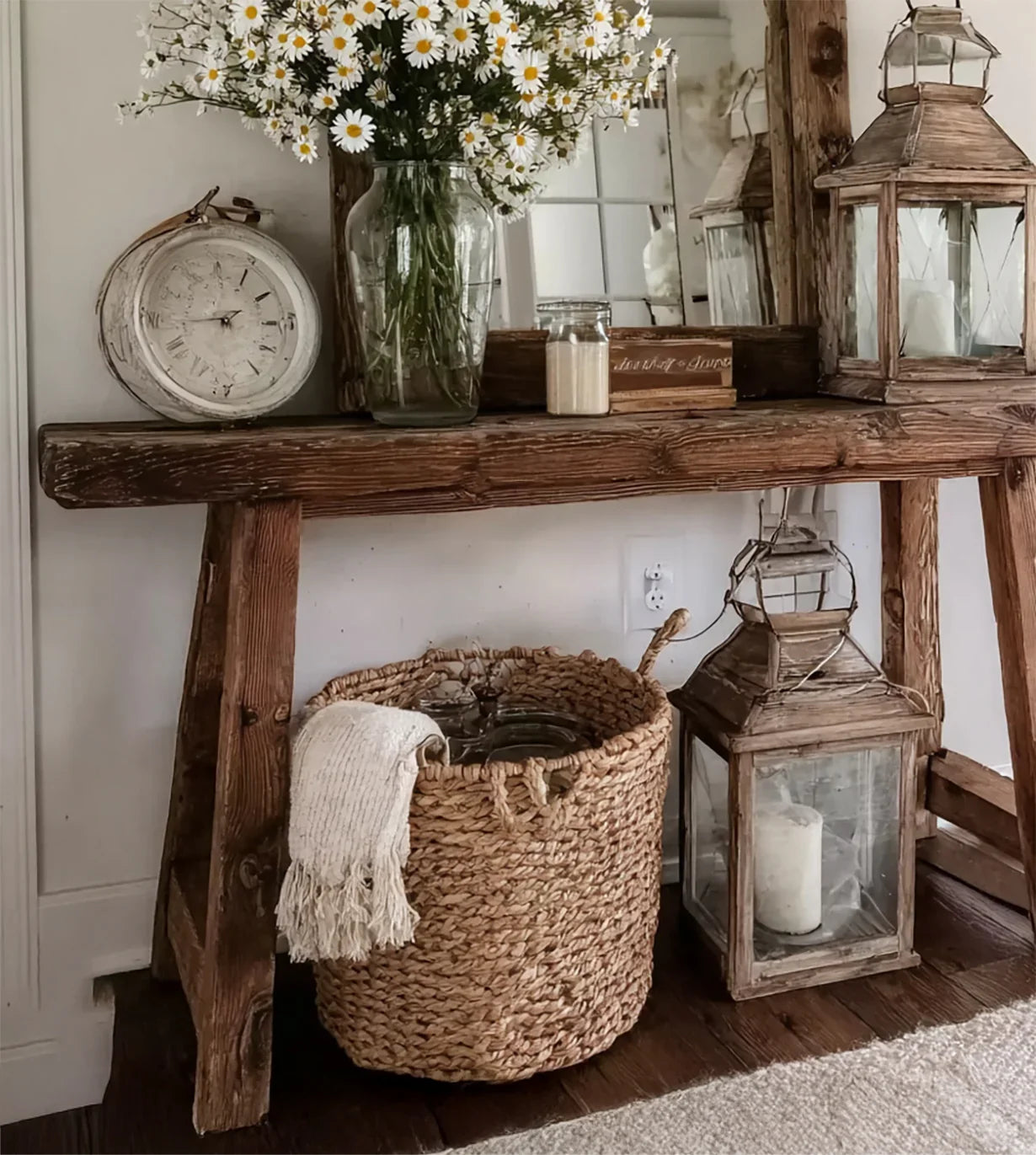 Rustic wooden console table with glass vase of daisies, vintage clock, wicker basket, and lantern candles