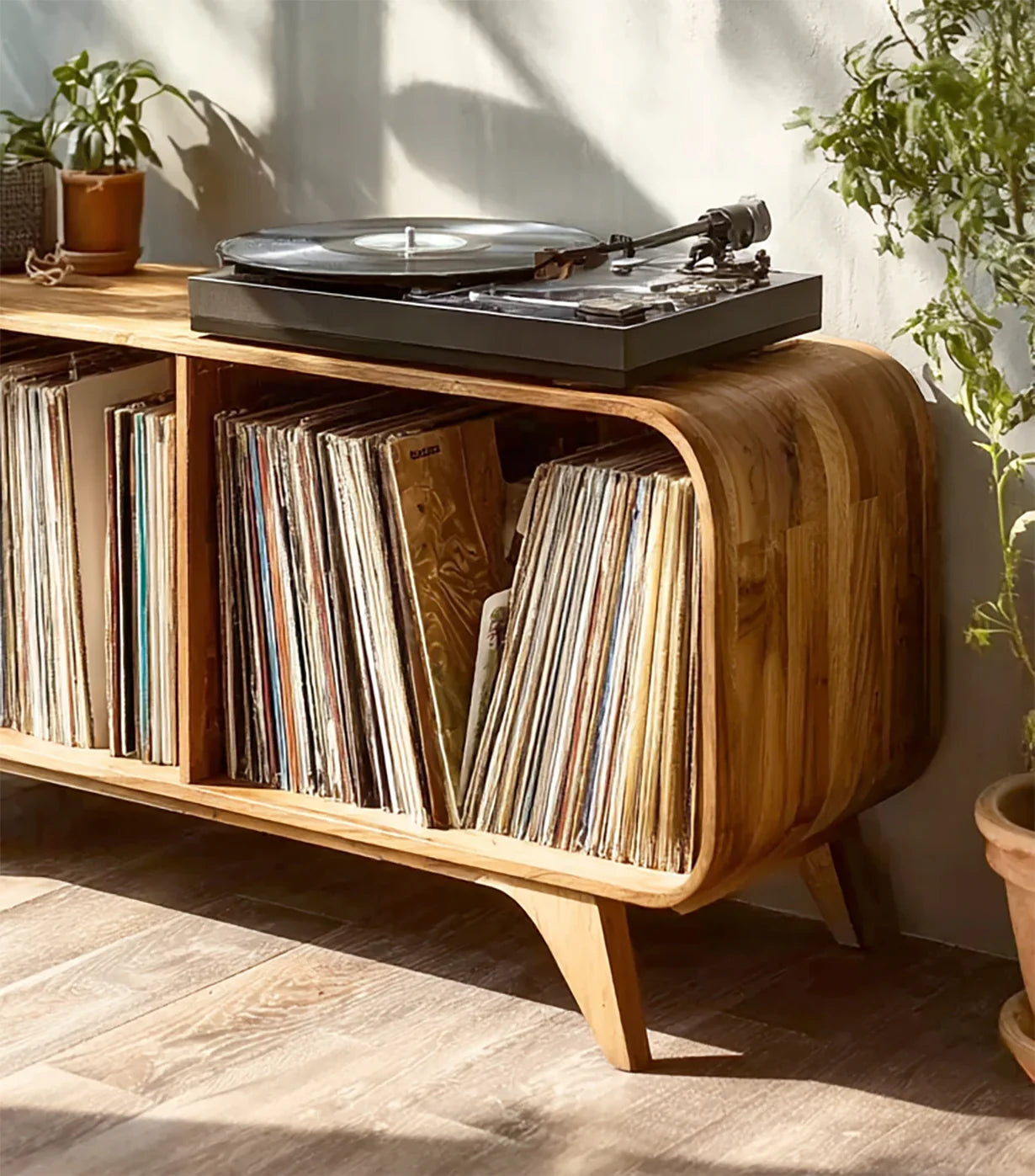 Modern wooden record player stand storing vinyl records, topped with a black turntable in sunny room