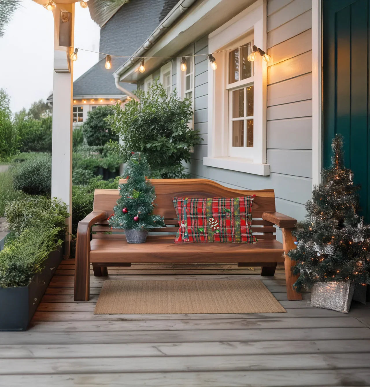 Wooden bench on porch with small decorated Christmas trees and plaid holiday pillow, string lights