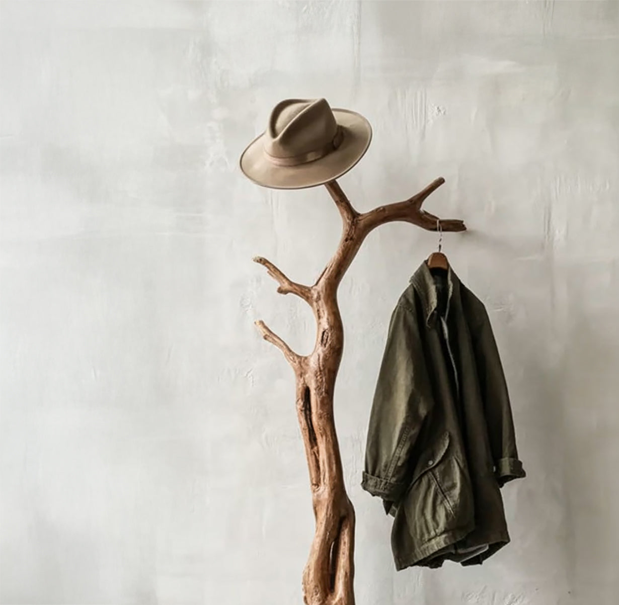 Live edge solid wood coat rack with jacket and hat against a light wall