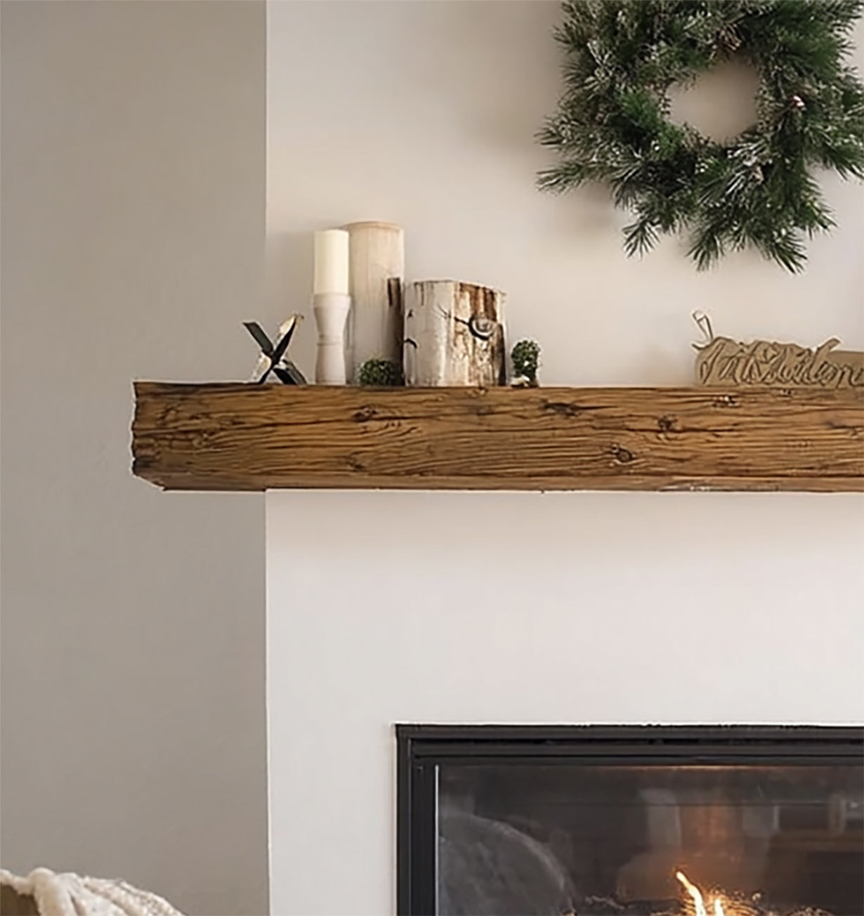 Rustic wooden mantle above fireplace decorated with candles, birch log pieces, and green wreath