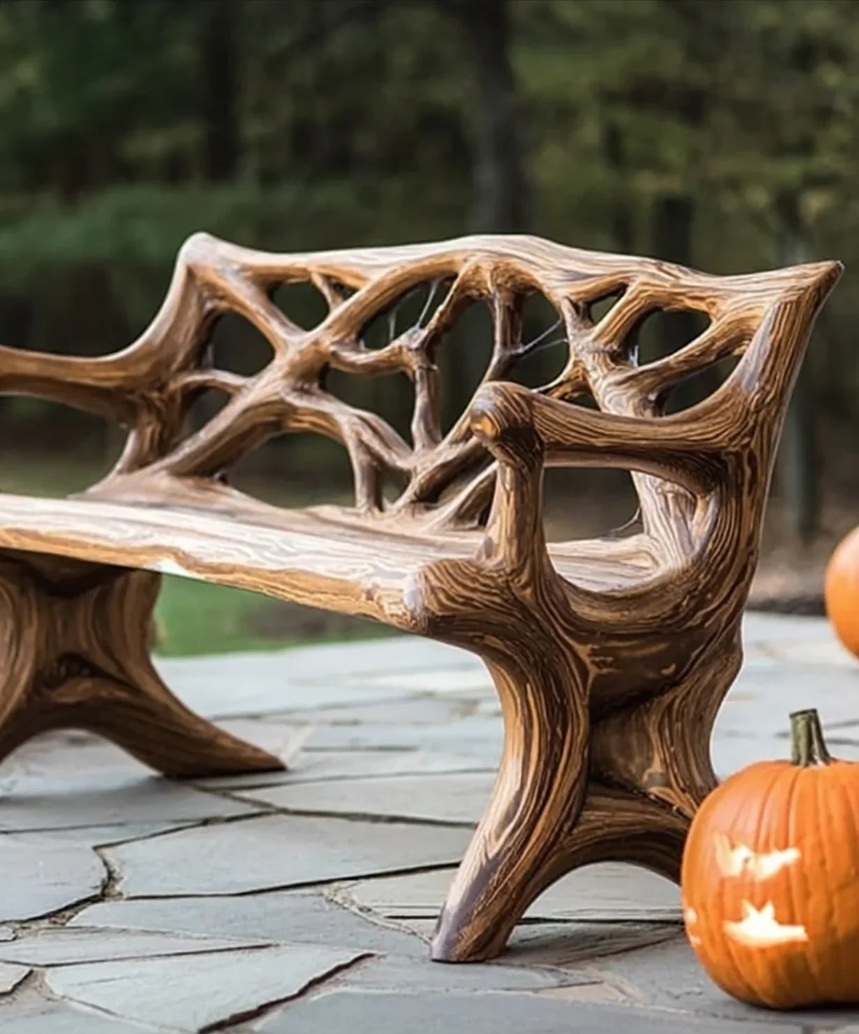 Rustic wooden bench with intricate branch design on stone patio, autumn outdoor setting with carved pumpkins