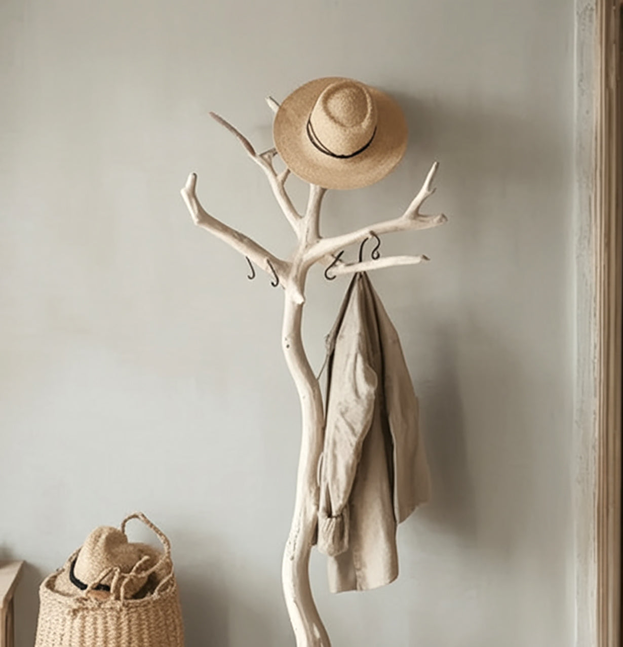 Beige coat and straw hat hanging on white wooden branch coat rack in minimalist room