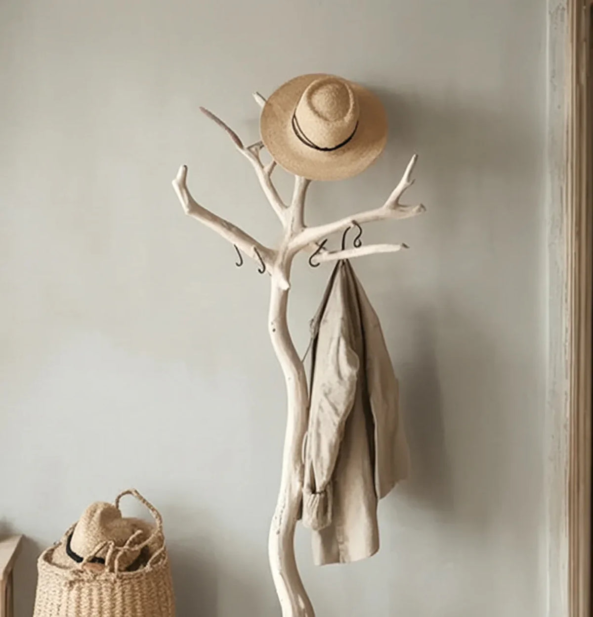 Beige coat and straw hat hanging on white wooden branch coat rack in minimalist room