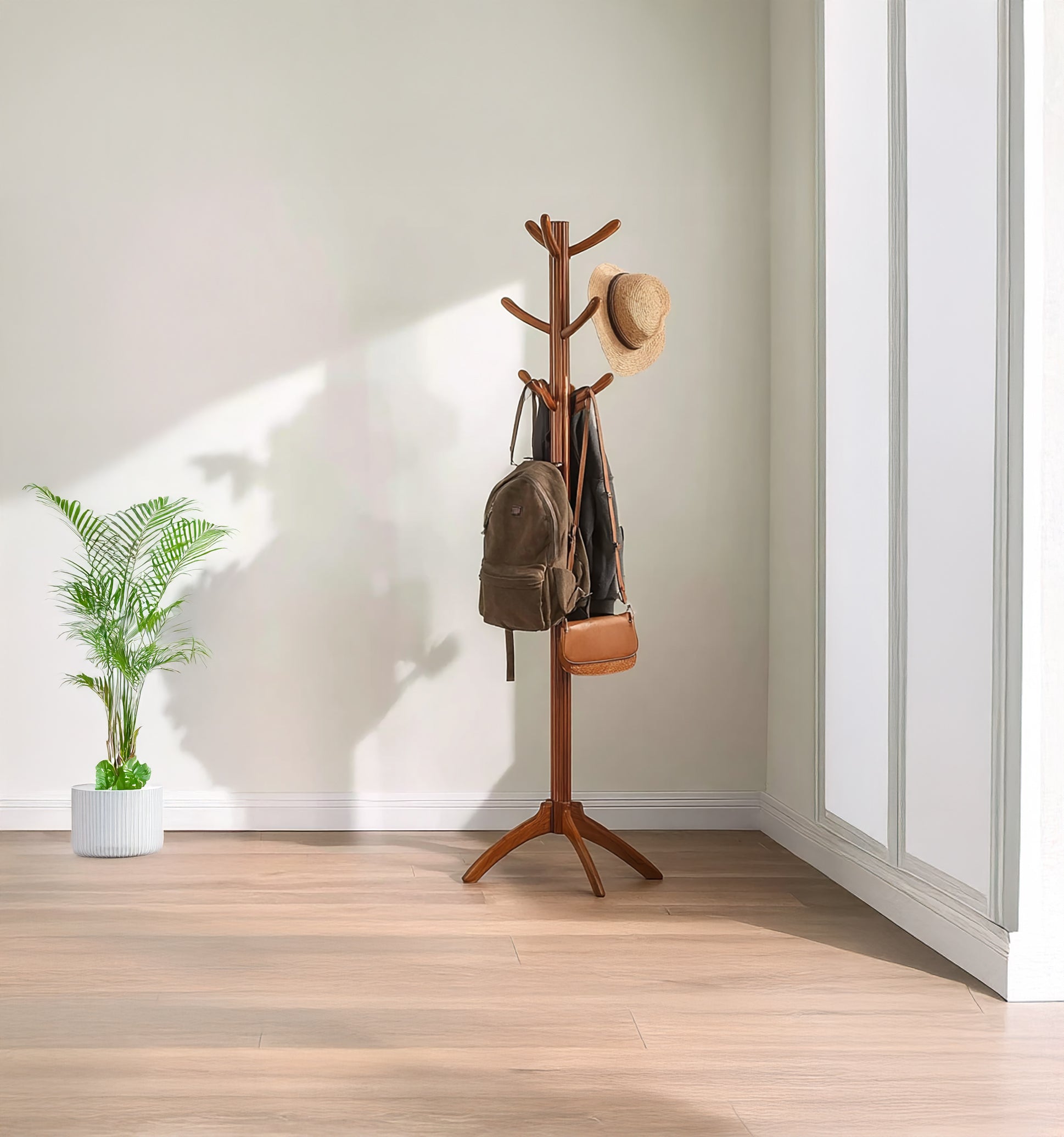 Wooden coat rack with hat, backpack, handbag in bright minimalist room with potted plant