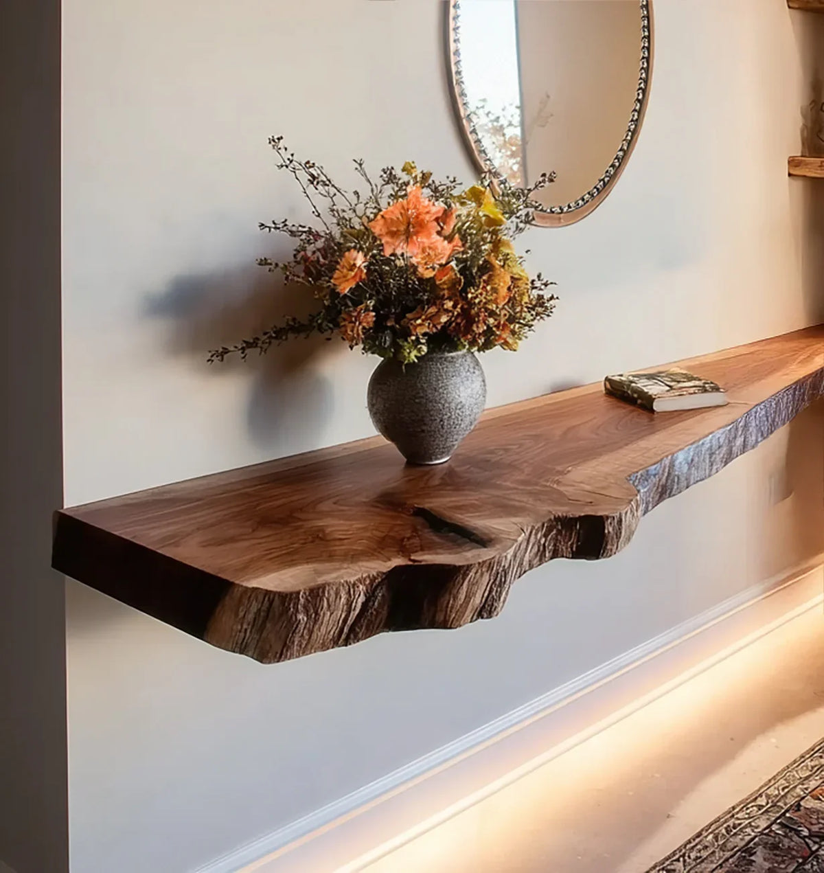 Live edge wood floating shelf with a gray vase of orange flowers and a book under oval mirror
