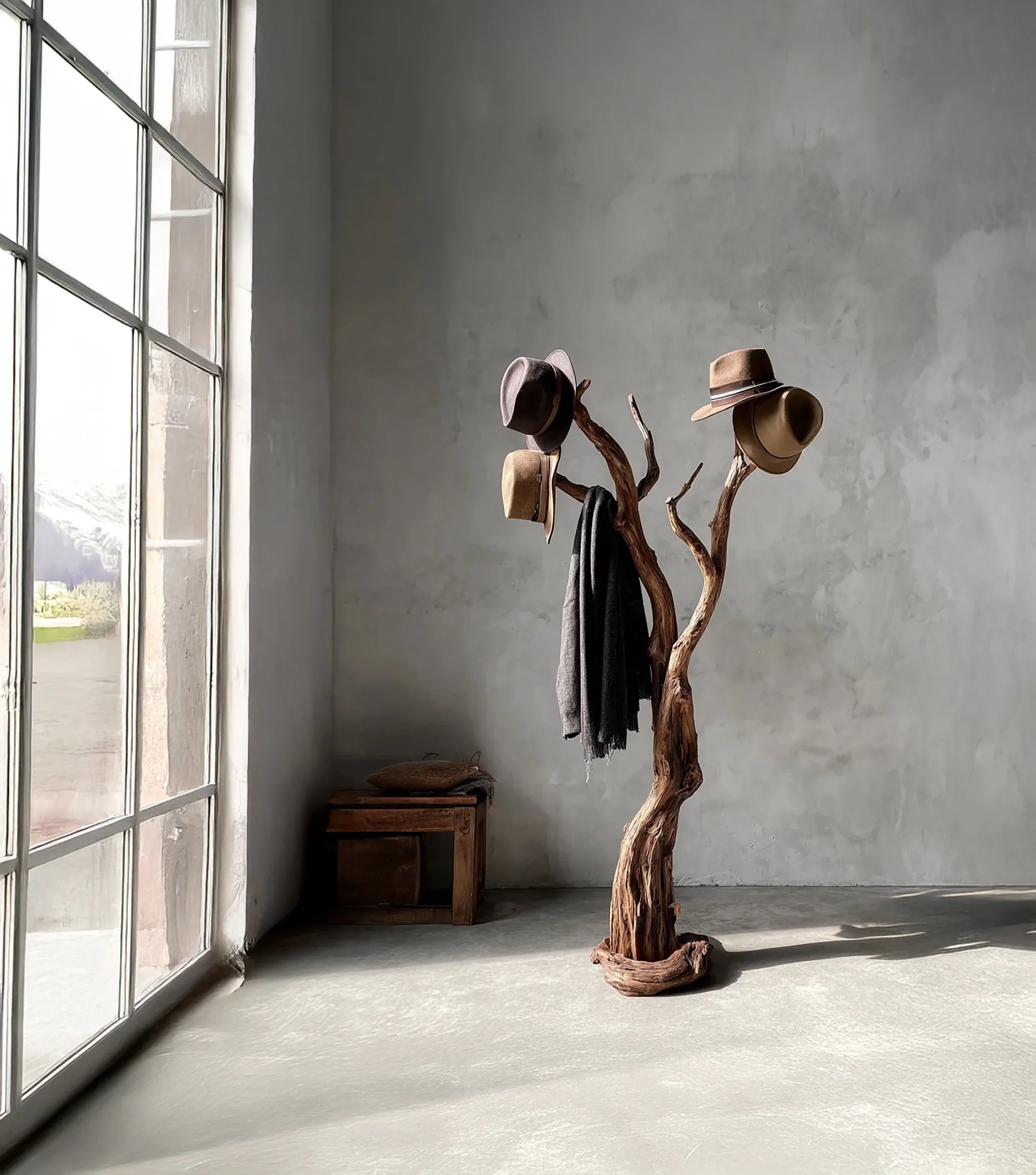 Rustic wooden coat rack holding hats and a scarf in a sunlit minimalist room with a large window