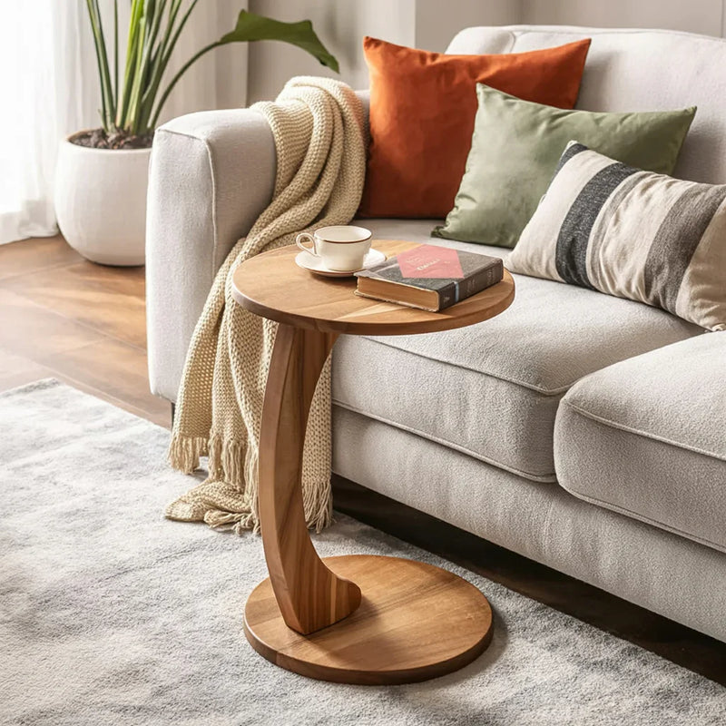 Solid wood side table with curved base beside sofa with throw pillows and cozy blanket in modern living room
