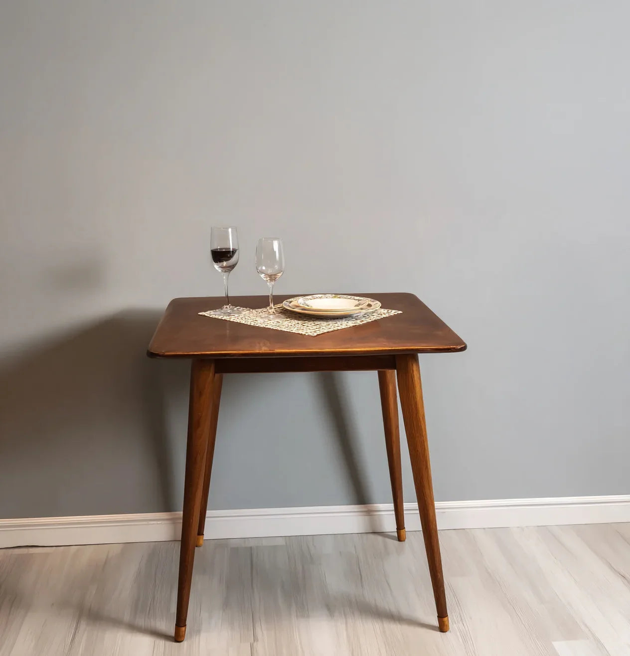 Solid wood dining table with tapered legs, set with wine glasses and plate on a mat