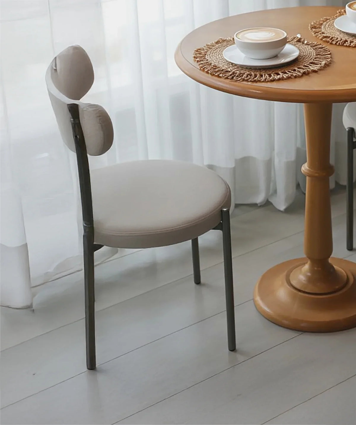 Modern upholstered dining chair beside round wooden table with coffee, airy room setting