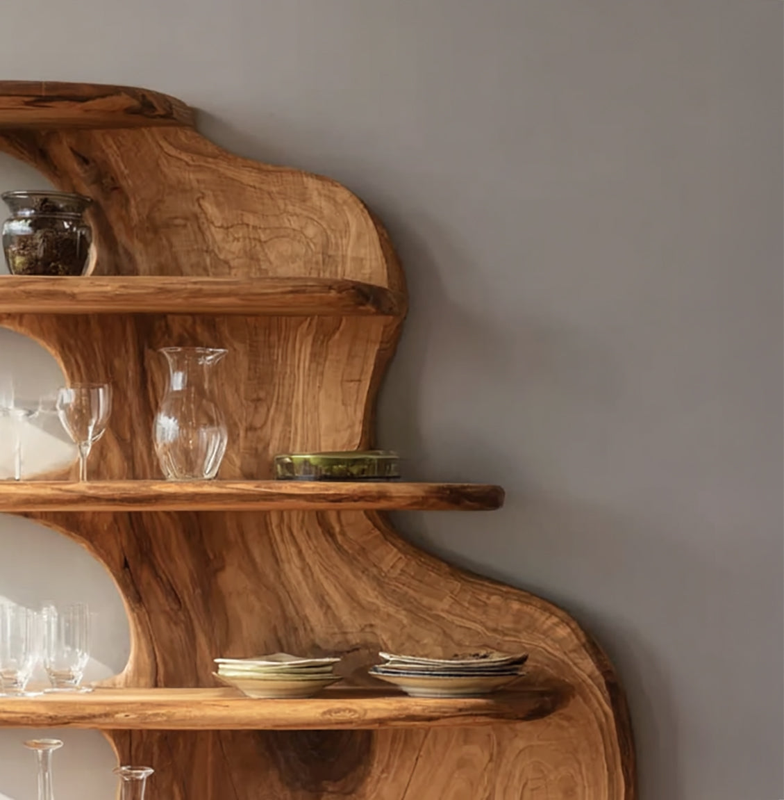 Rustic wooden wall shelf with glassware and ceramic plates against gray wall