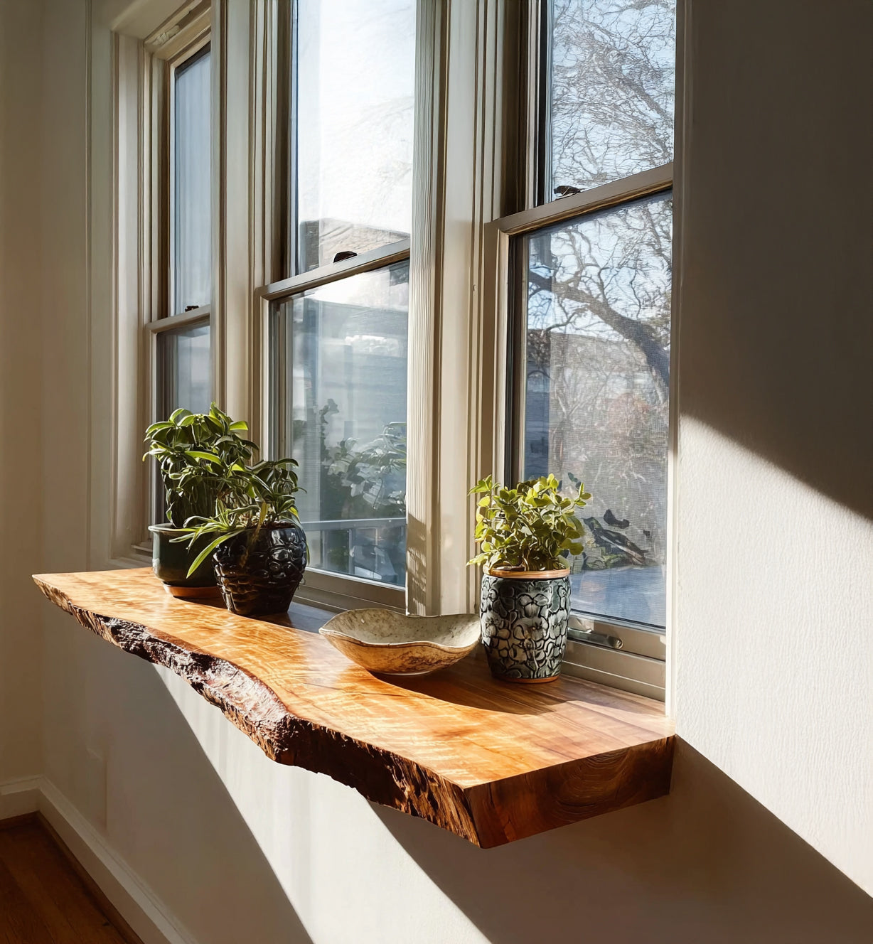Natural live edge wooden window shelf with potted plants and ceramic bowl in bright sunlight