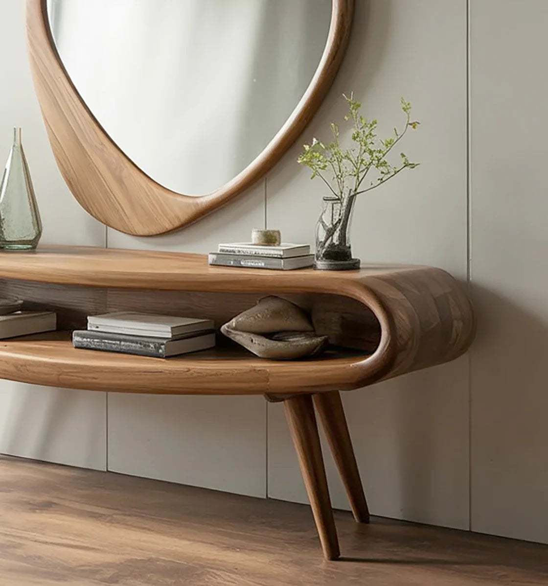 Curved wooden console table with books and decorative items under a large oval wood-framed mirror