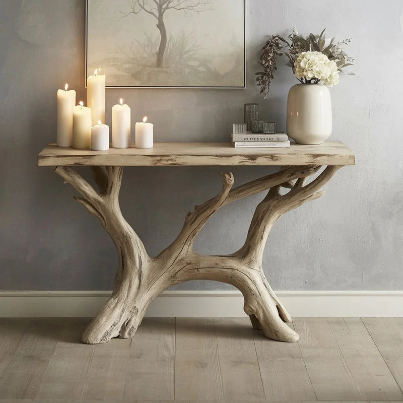 Rustic driftwood console table with lit candles, books, glassware, and vase with white flowers in minimalist room