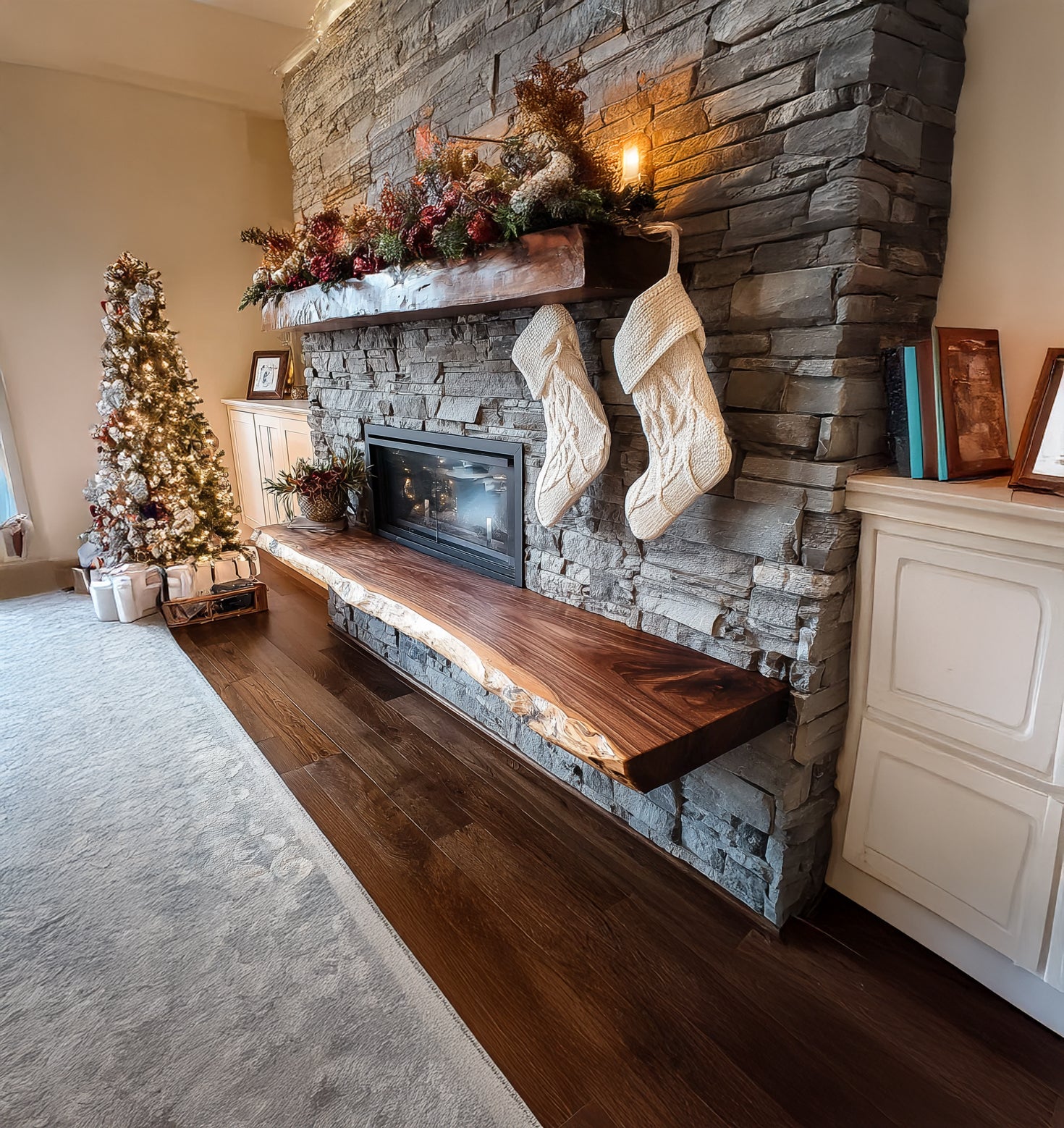 Cozy living room with stone fireplace, wooden mantel, hanging knit Christmas stockings, decorated tree, and hardwood flooring