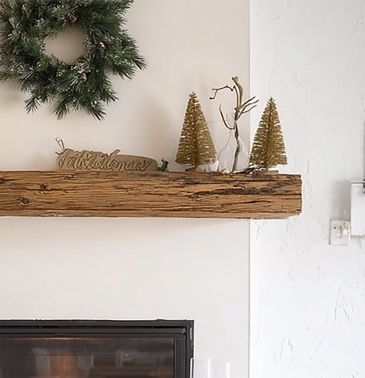 Rustic wooden mantel decorated with glittery gold Christmas trees, a green wreath, and a 'Christmas' sign