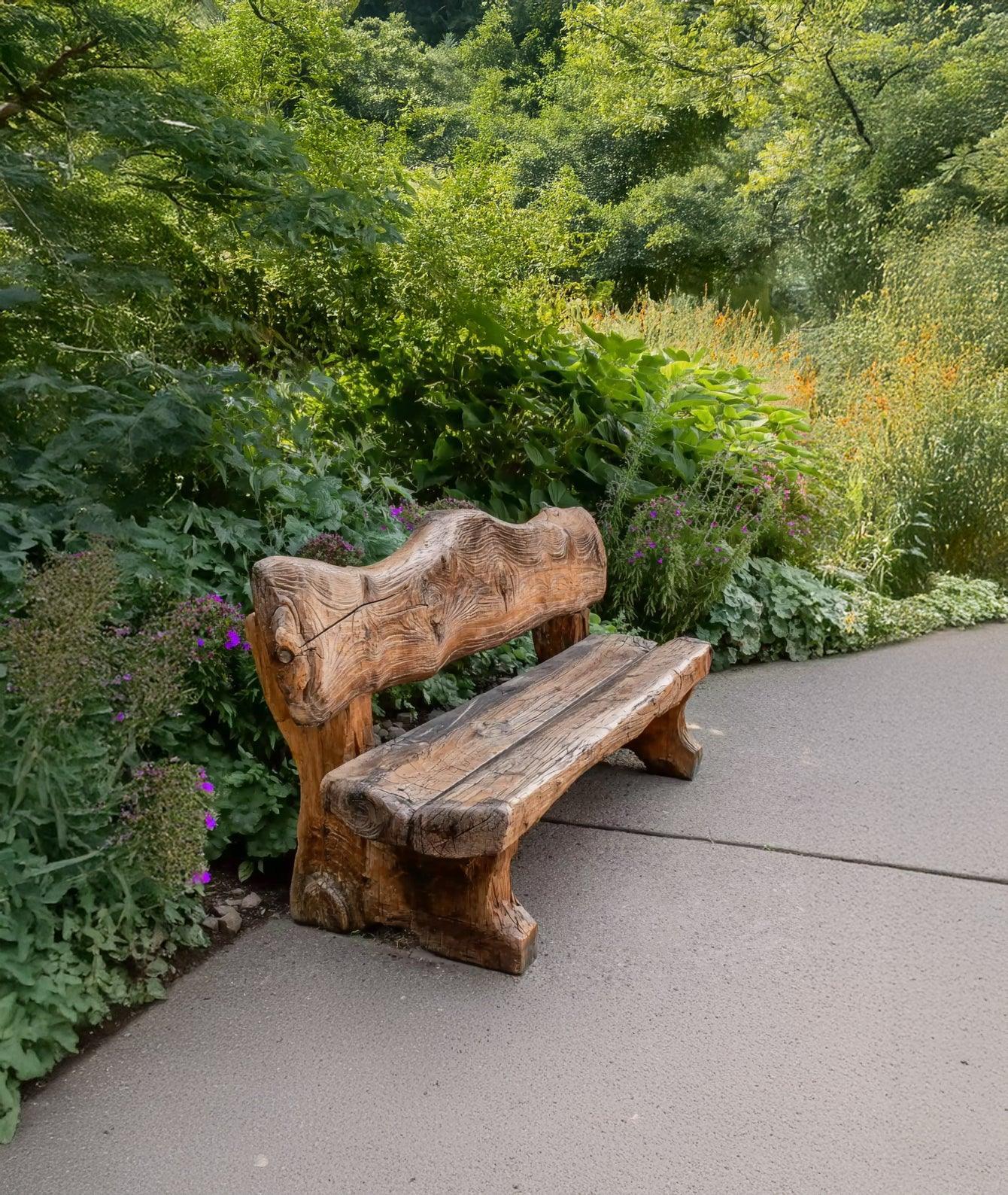 Handcrafted wooden bench on garden path surrounded by green plants and colorful flowers