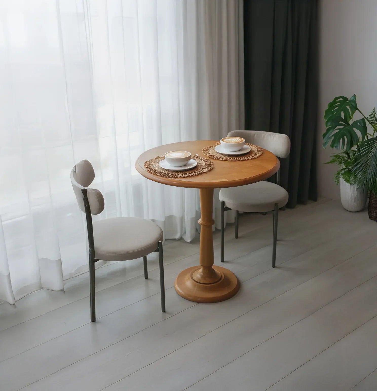 Round solid wood table with two chairs in modern dining room, coffee cups on placemats