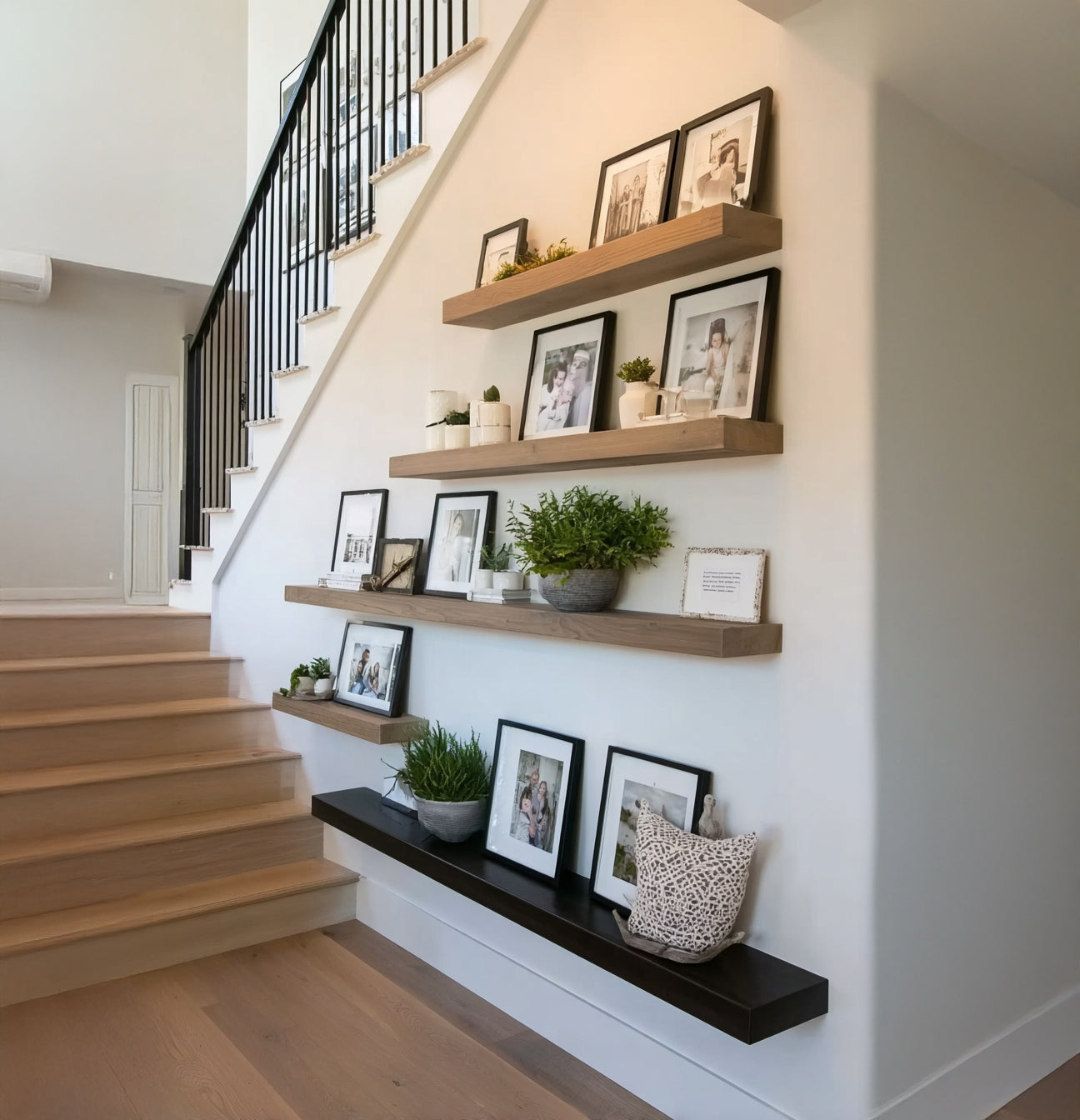 Modern staircase with wooden steps and black railing, decorated with floating shelves holding framed photos and green plants
