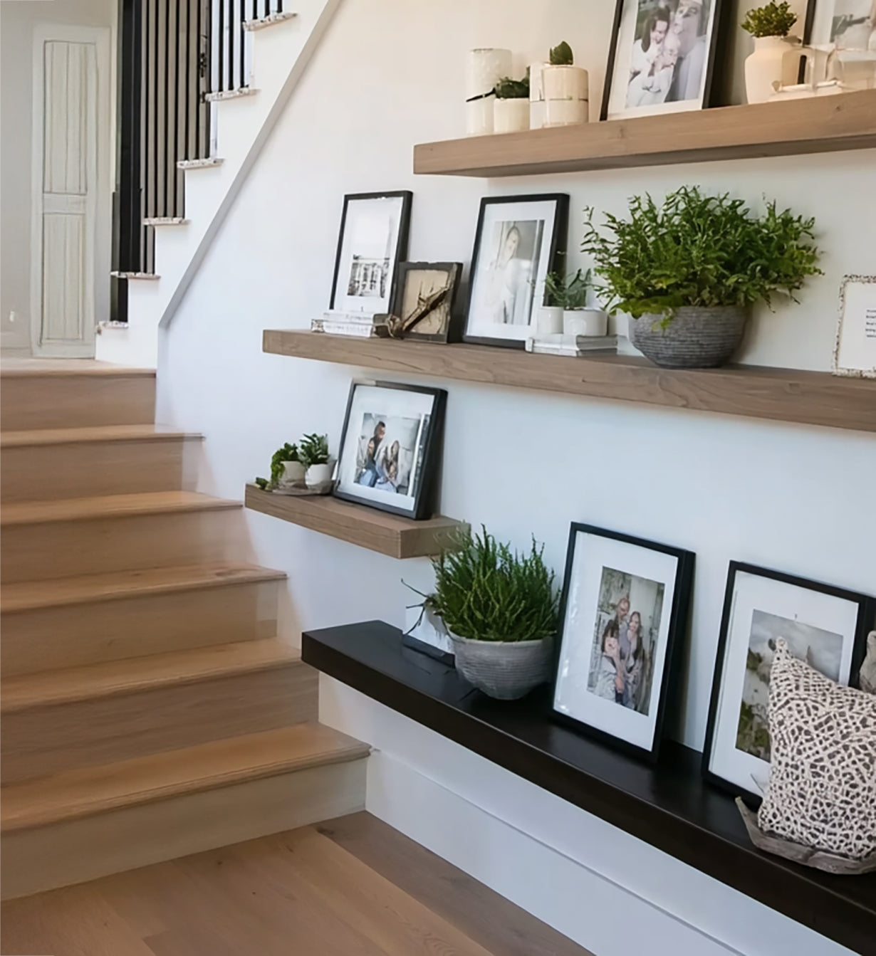 Wooden stairs next to decorative floating shelves with potted plants and framed photos in modern home