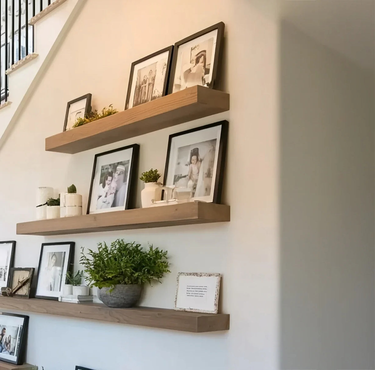 Modern wall with wooden floating shelves displaying framed photos, plants, and decorative items