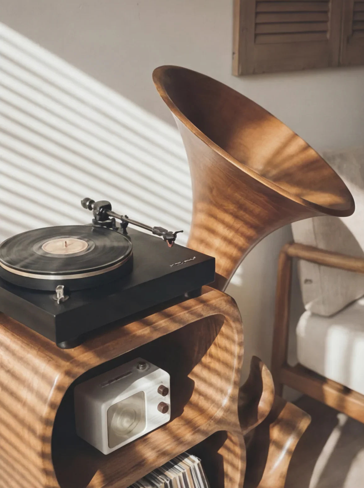 Modern solid wood gramophone-style speaker stand with vinyl turntable in sunlit room