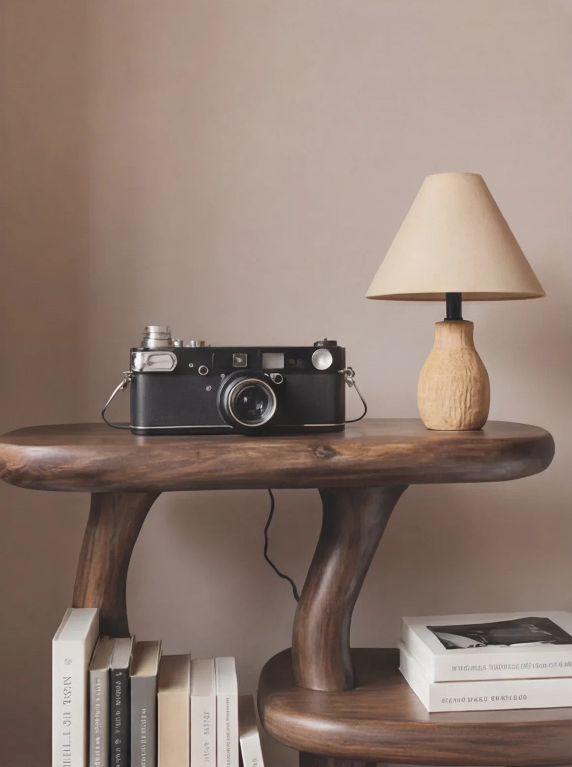 Solid wood live edge side table with books, vintage camera, and small lamp in a minimal room