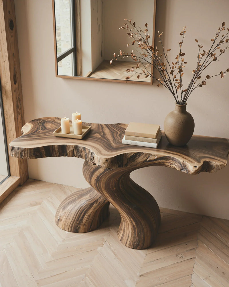 Live edge solid wood console table with sculpted base, candles, books, and ceramic vase.