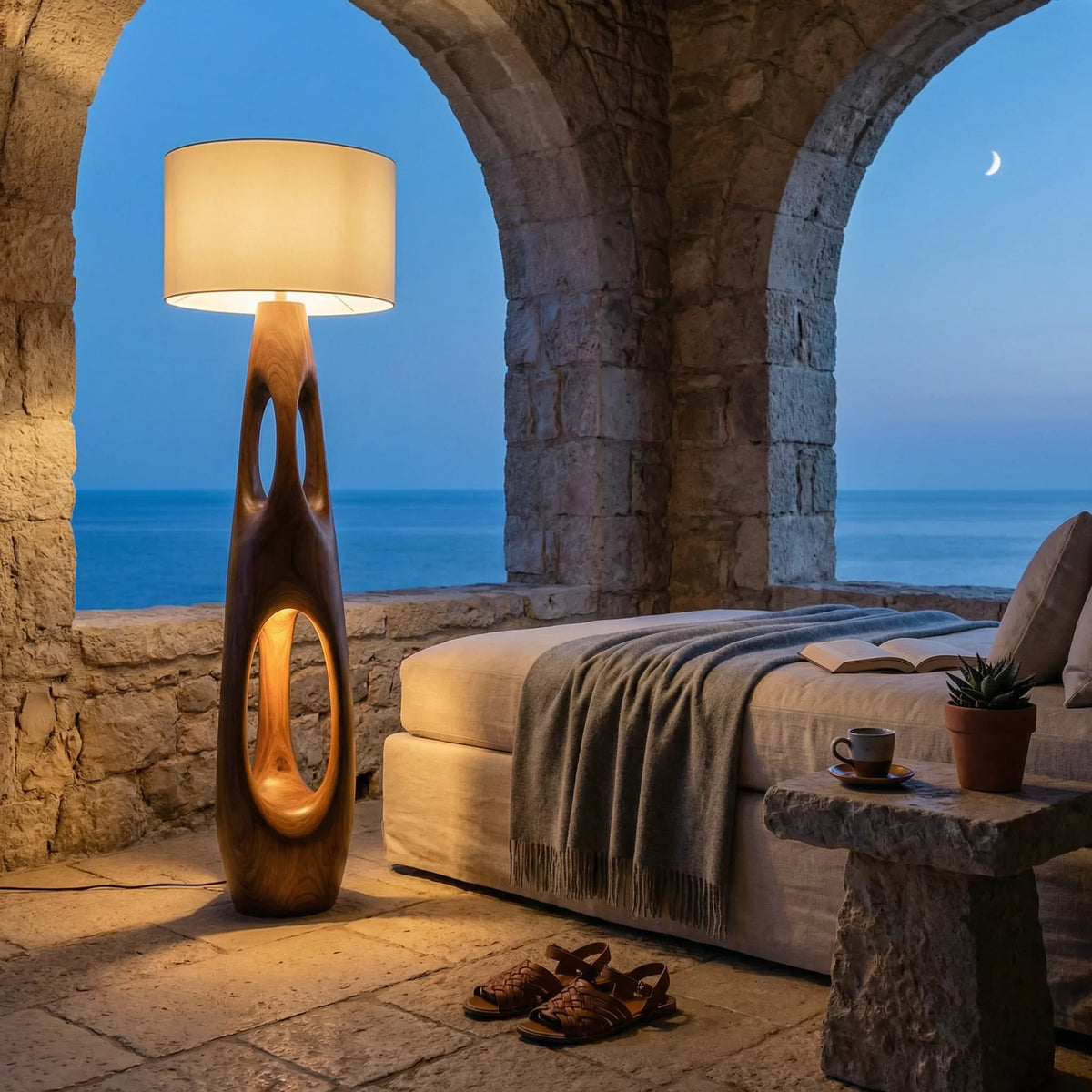 Carved solid wood floor lamp with dual openings in a cozy stone room overlooking the ocean at dusk