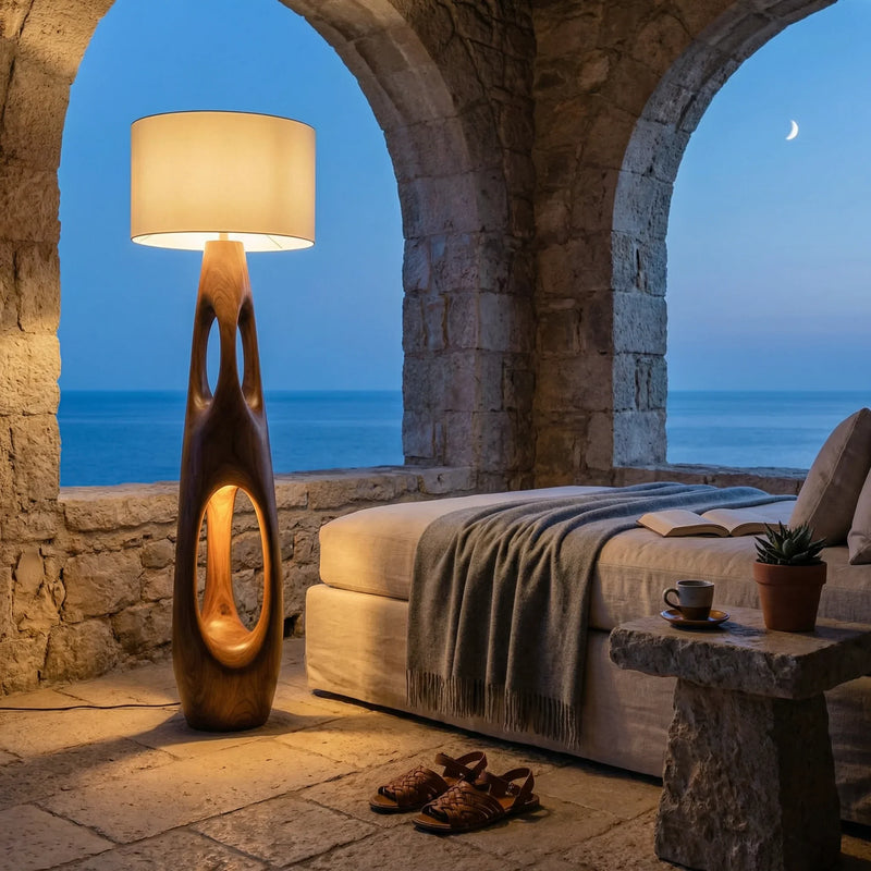 Carved solid wood floor lamp with dual openings in a cozy stone room overlooking the ocean at dusk