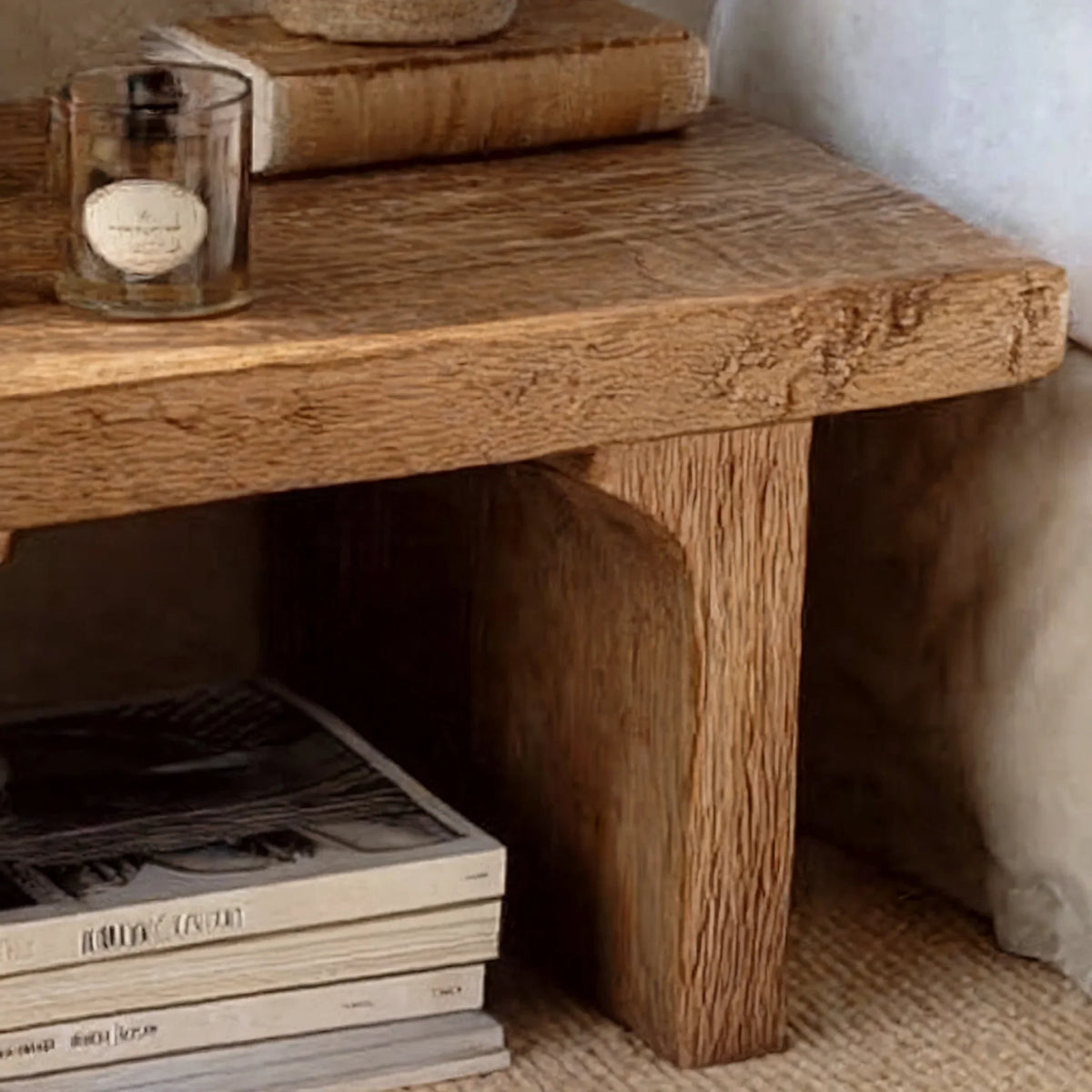 Close-up of a rustic solid wood side table with textured grain and stacked books on a shelf.