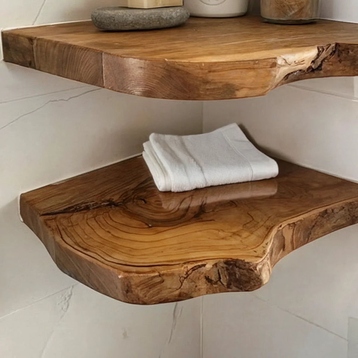 Close-up of two live edge floating wood shelves in a corner, one with folded white towel