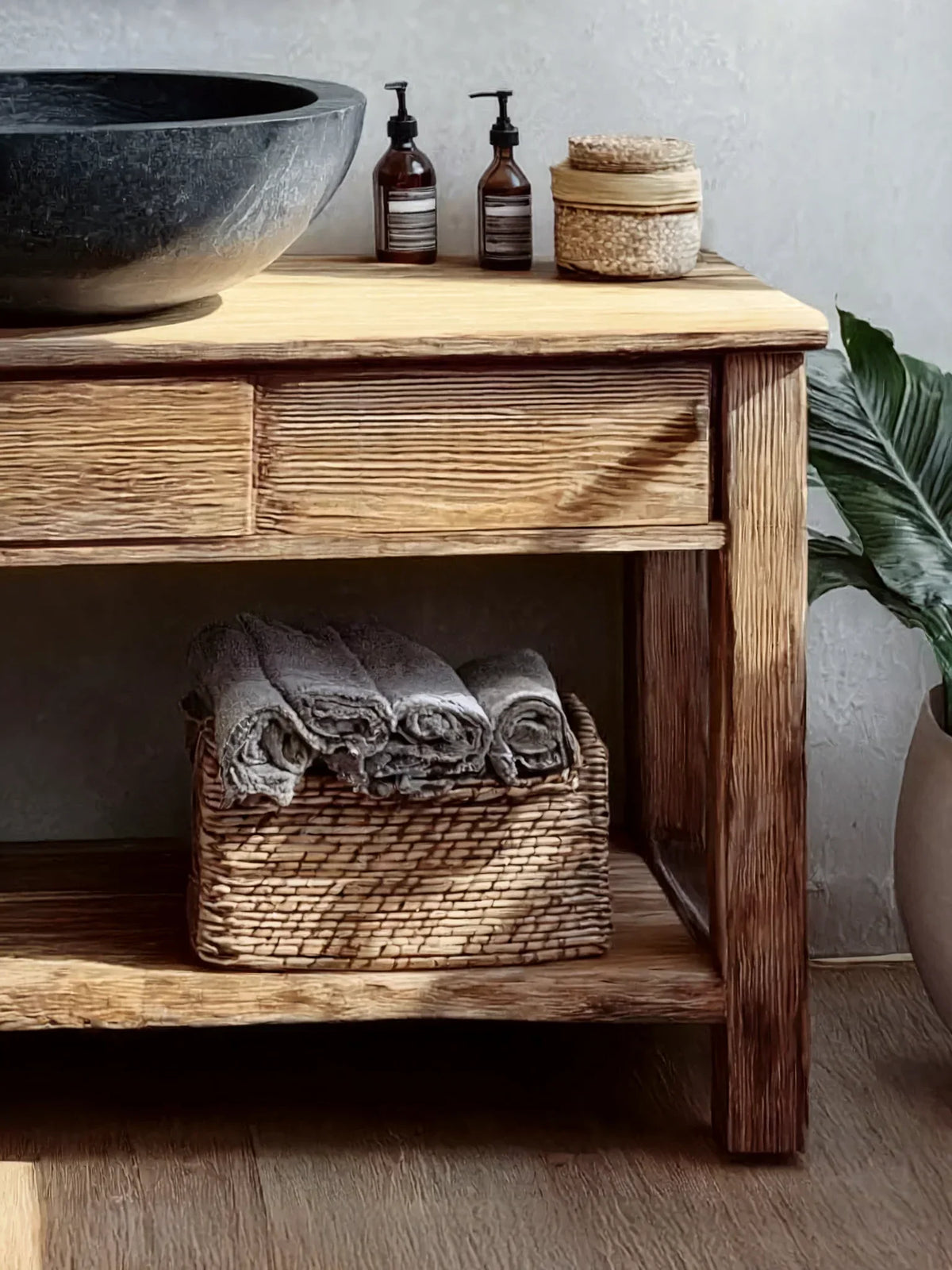 Rustic wooden bathroom vanity with stone sink, woven basket, and rolled towels