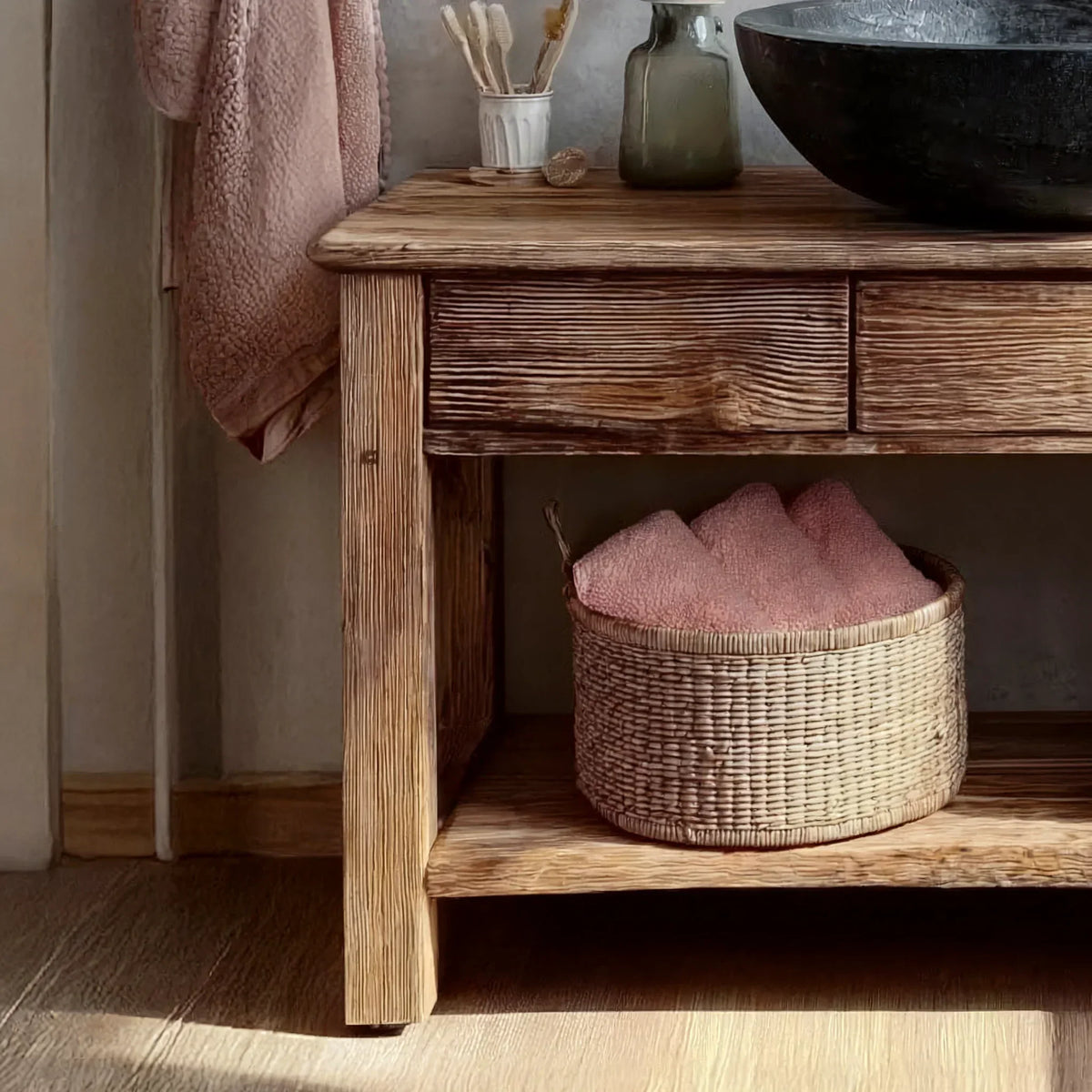 Rustic wooden console table with drawers, woven basket, and pink towels in a cozy setting