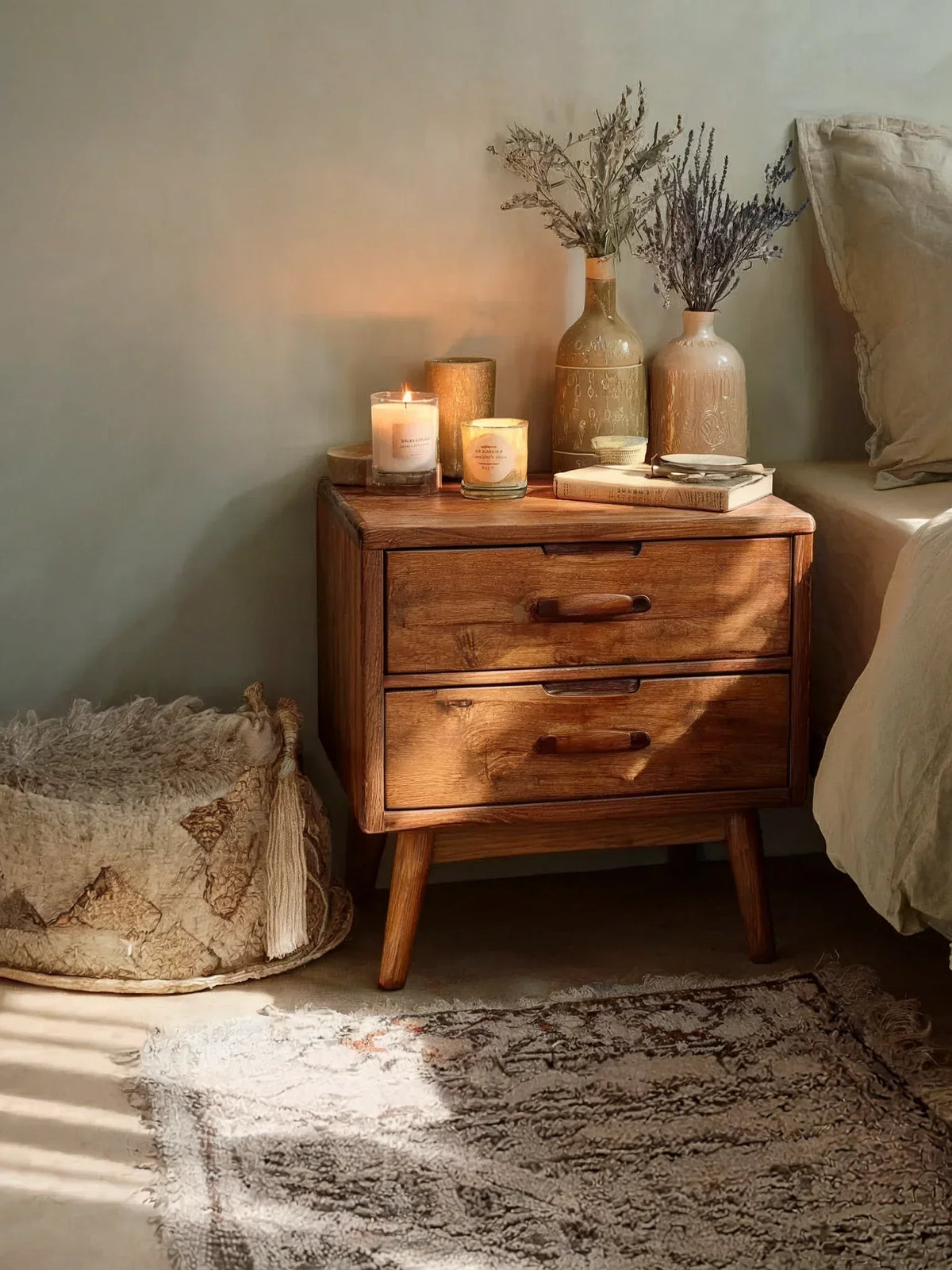 Cozy bedroom corner with a solid wood nightstand, candles, ceramic vases, and textured rug