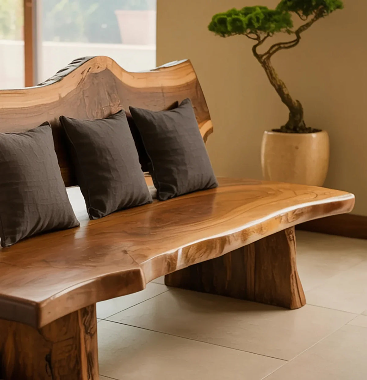 Live edge solid wood bench with black cushions in modern room, potted bonsai in background