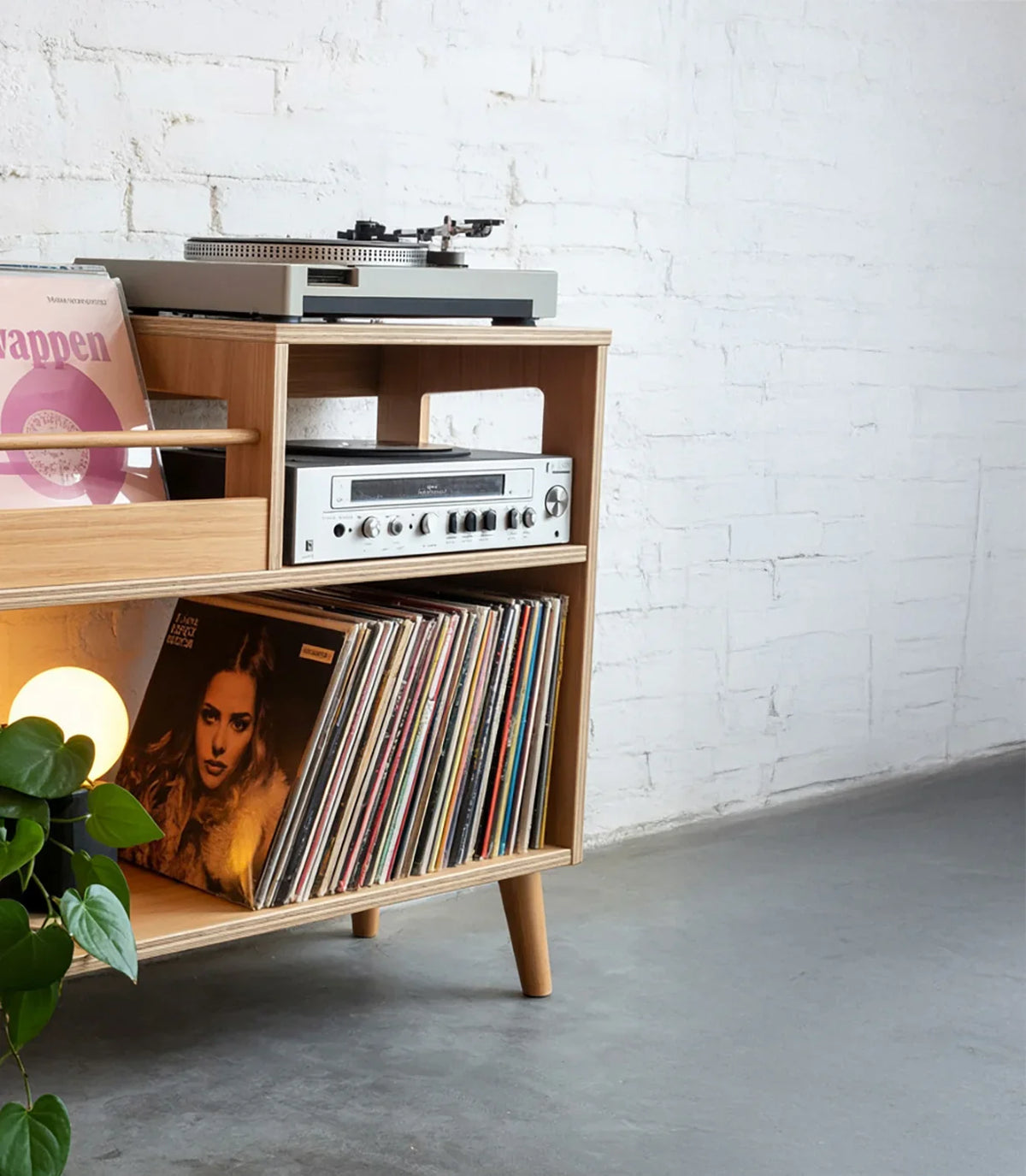 Wooden mid-century modern record player stand with turntable, speakers, vinyl records, and green plant