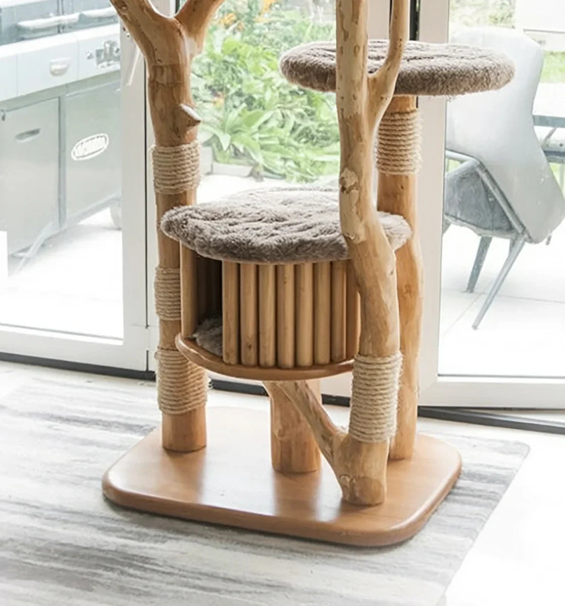 Natural wood cat tree with beige plush platforms and rope-wrapped posts in bright room