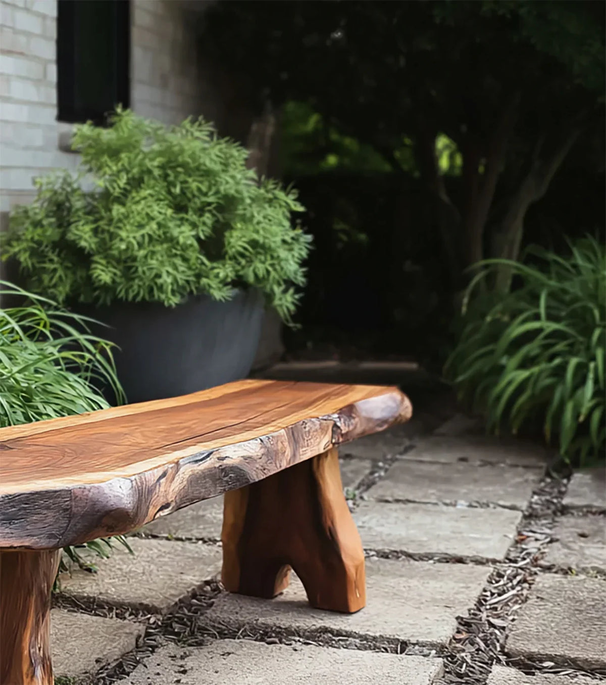 Handcrafted live edge wooden bench on stone patio surrounded by green potted plants and foliage