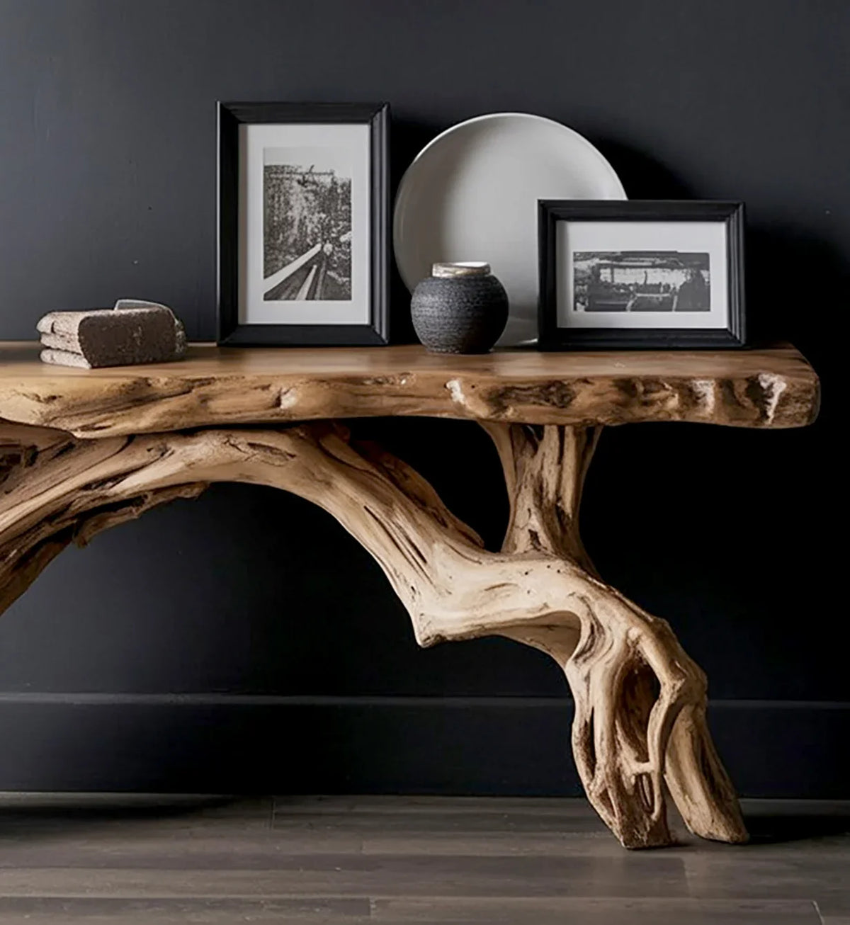 Rustic wooden table with natural tree root design against dark wall, decorated with framed photos and pottery