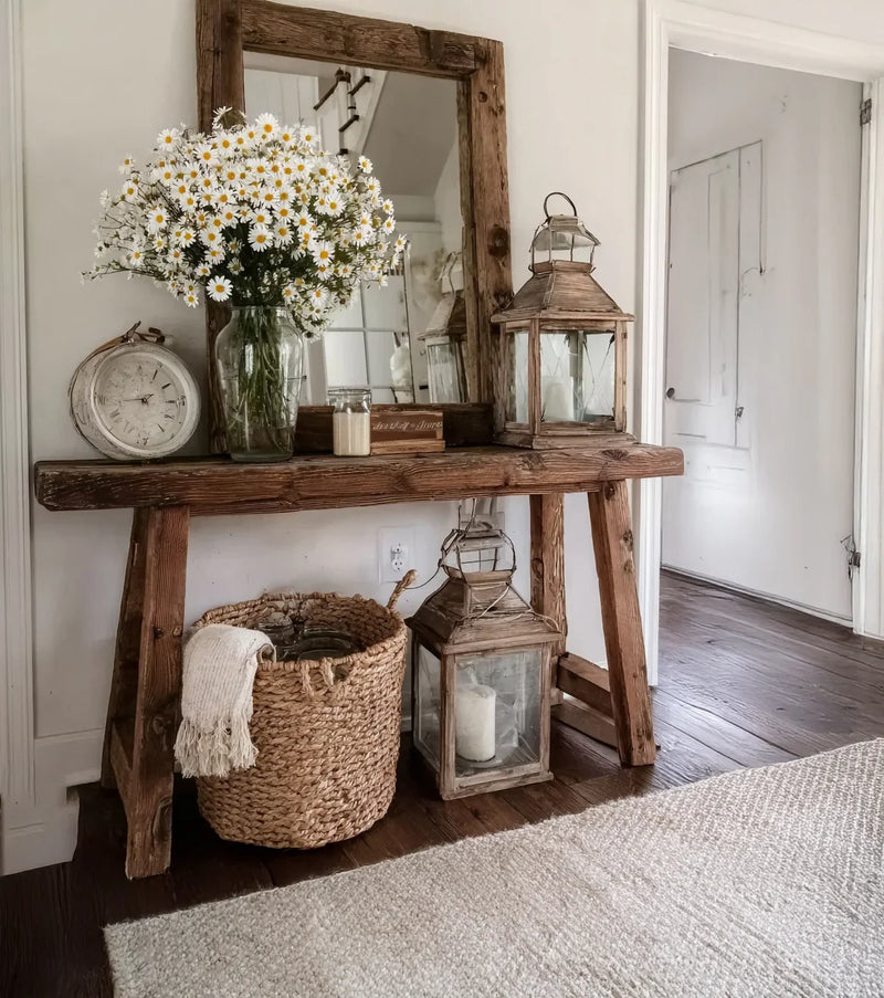 Rustic wooden console table with daisy bouquet, vintage clock, lanterns, woven basket, and mirror in cozy hallway