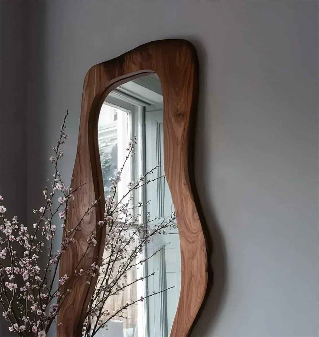 Live edge solid wood mirror on gray wall beside window and blooming branches