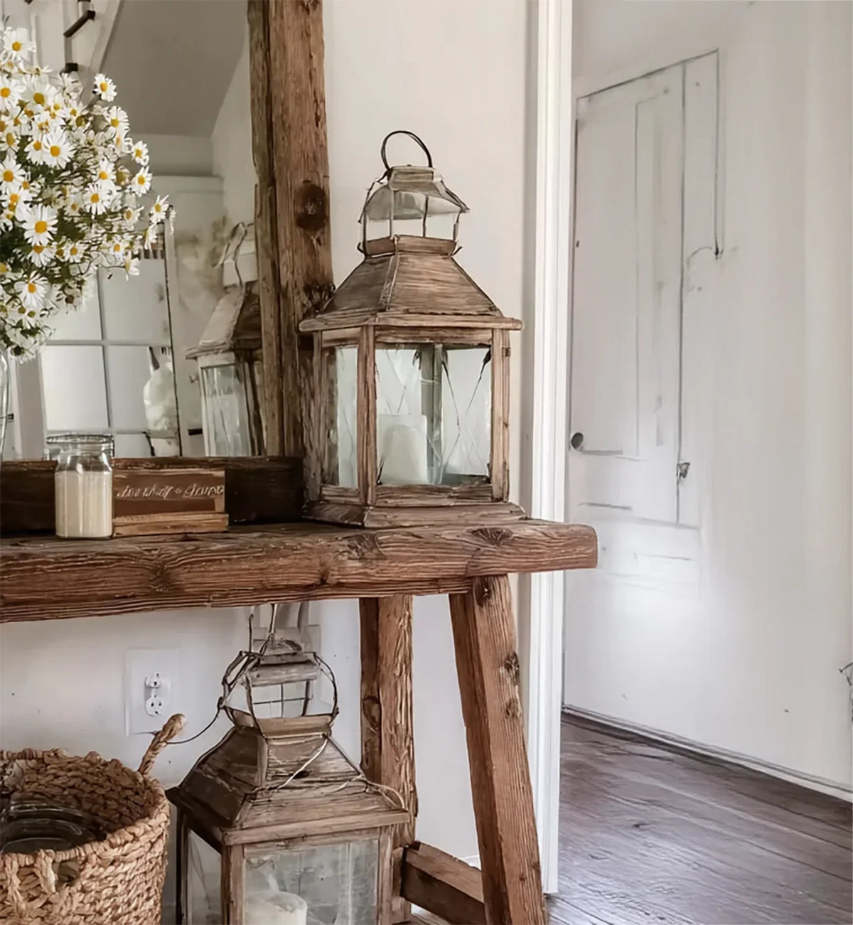 Rustic wooden table with decorative lanterns, daisies in vase, and vintage mirror in cozy room