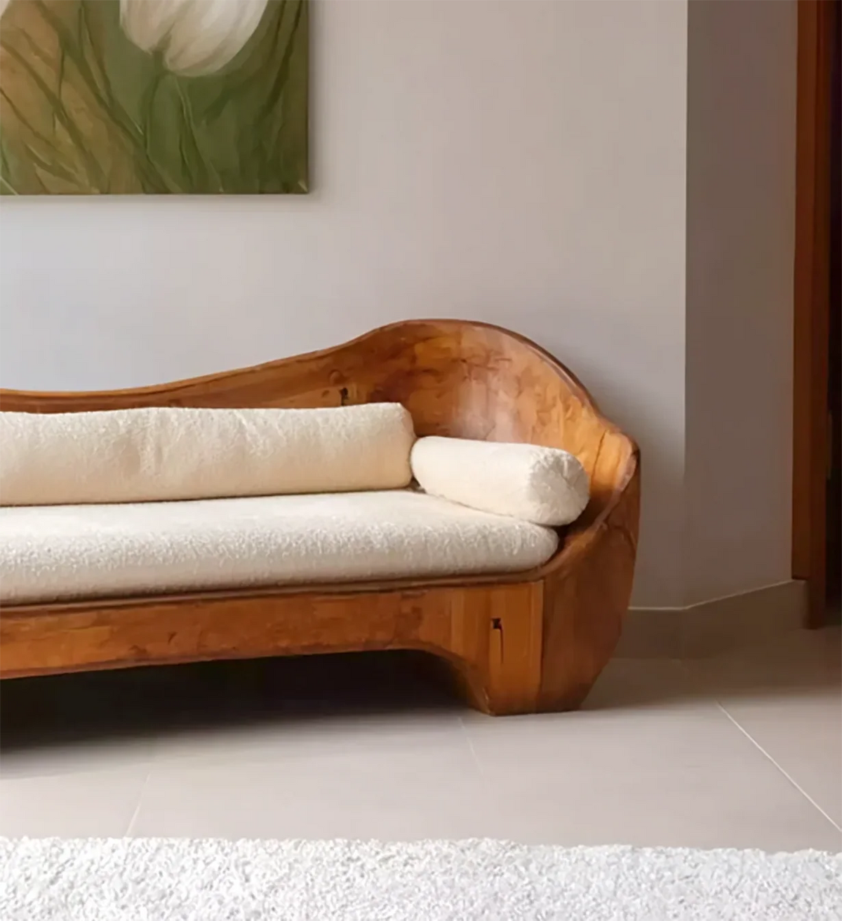 Wooden sofa with curved design and white textured cushions in a minimalistic living room