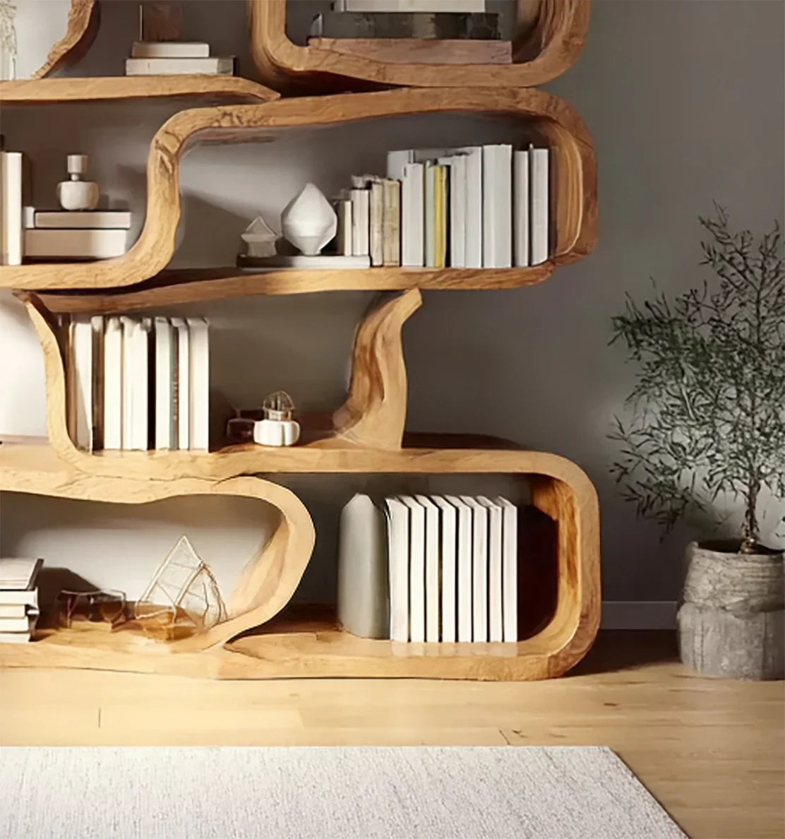 Modern wooden bookshelf with curved design, filled with white and beige books, decorative objects, and a potted plant nearby
