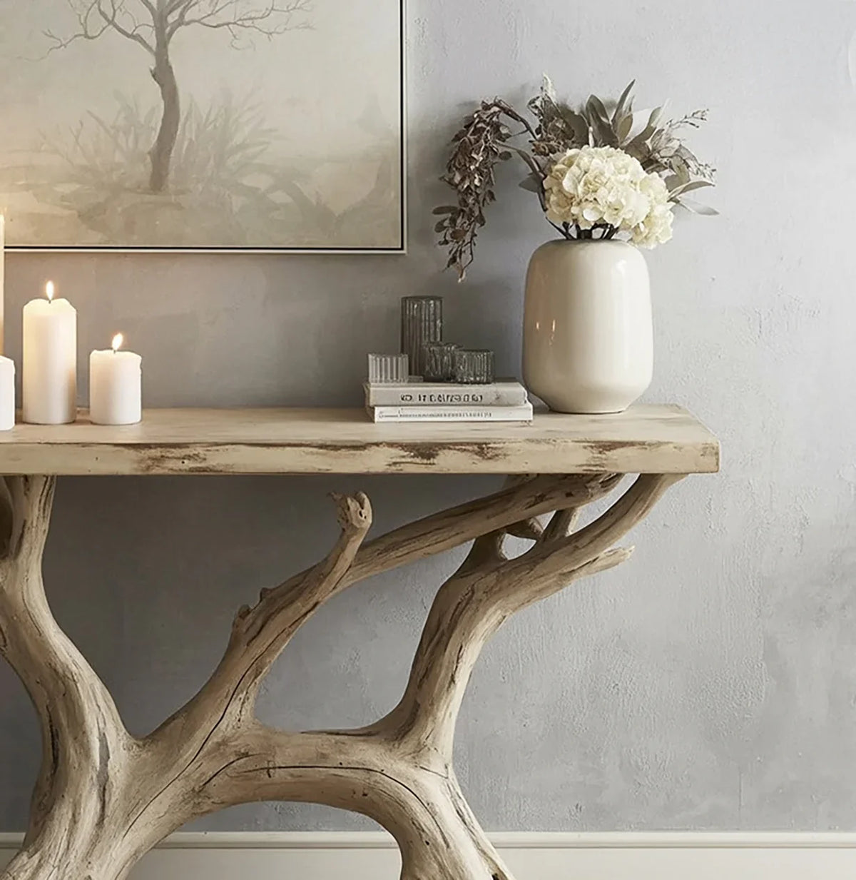 Natural wood branch console table with white candles, books, glassware, and cream floral vase